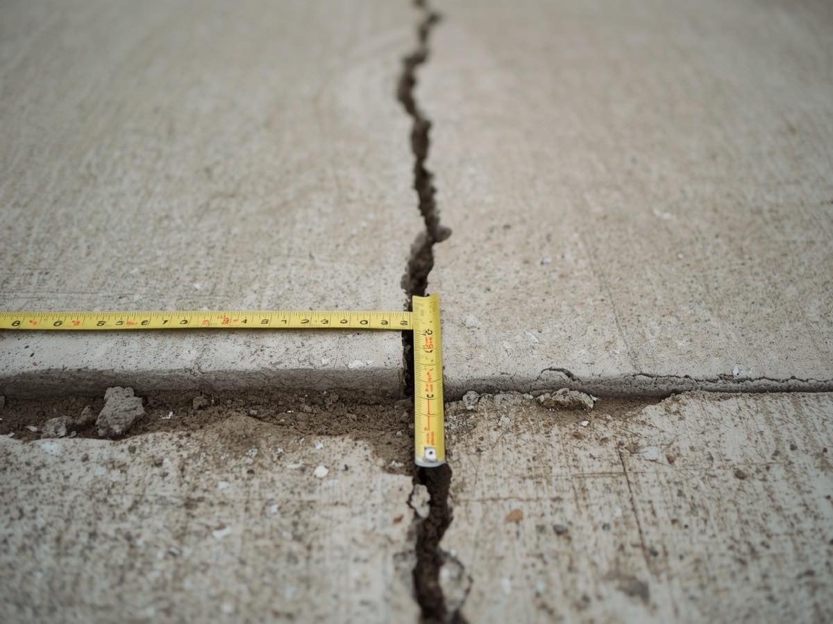 Tape measure showing the settlement height difference across a concrete driveway joint